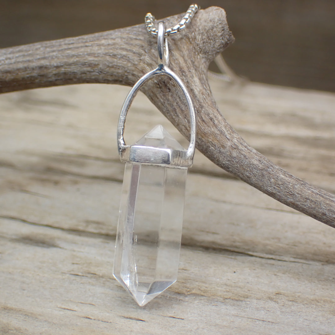 clear quartz crystal pendant photographed on driftwood