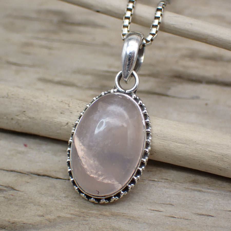 oval sterling silver rose quartz pendant photographed on driftwood