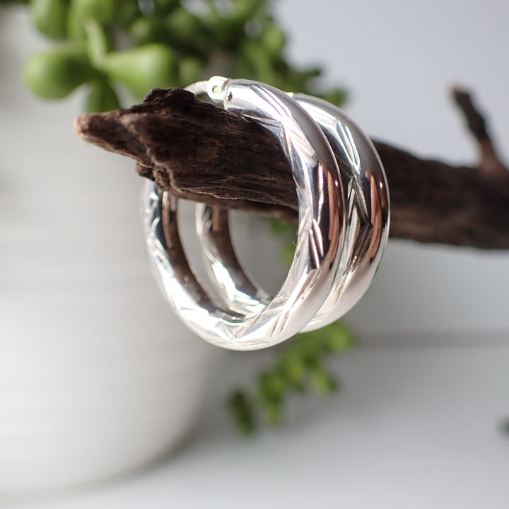 sterling silver open etched design hoop earrings hanging on driftwood