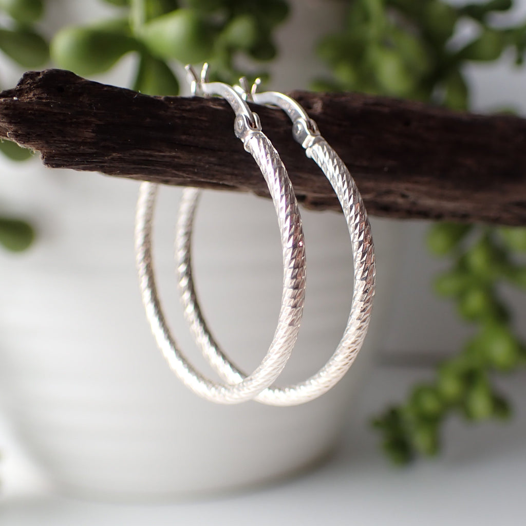 sterling silver patterned open hoop earrings hanging on driftwood