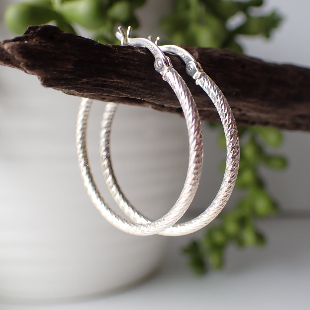 sterling silver patterned open hoop earrings hanging on driftwood