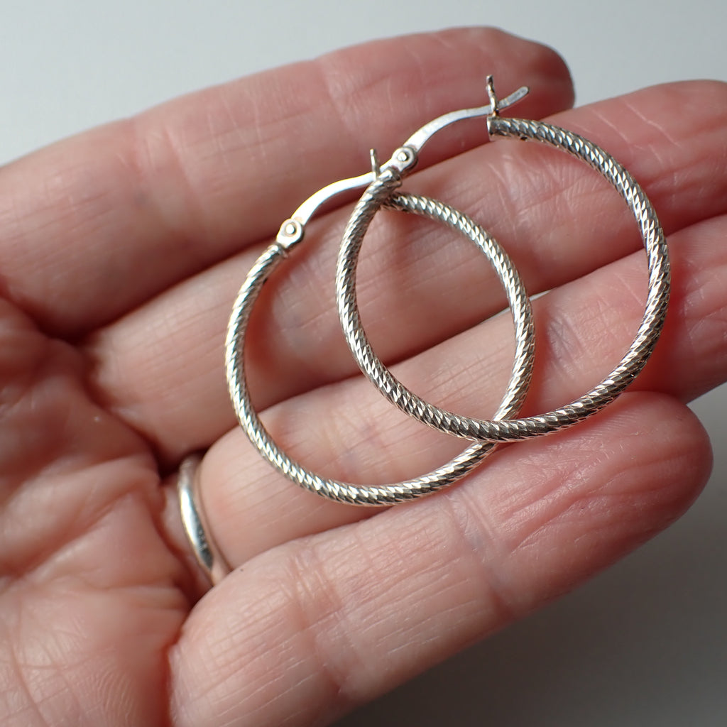 sterling silver patterned open hoop earrings hanging on driftwood